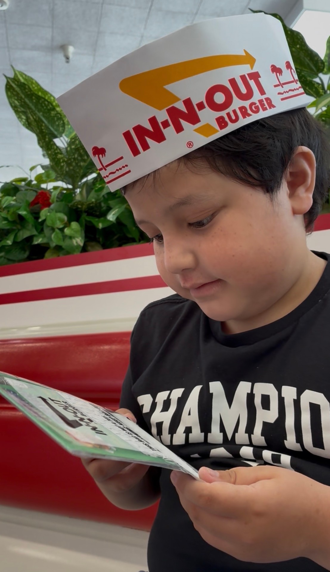 Lucian reading an In-N-Out activity menu while wearing the iconic paper hat