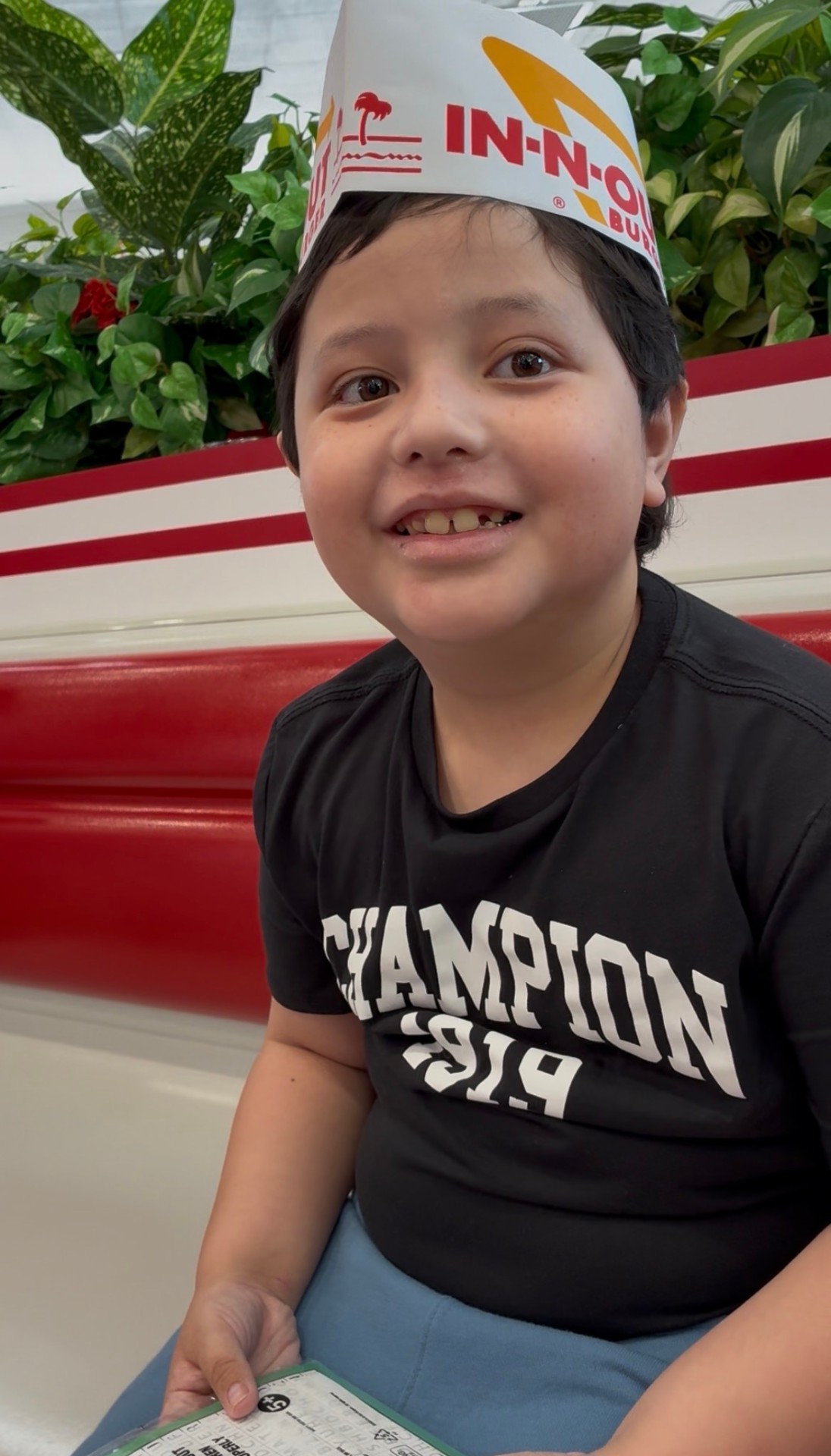 Lucian smiling in an In-N-Out paper hat at a red booth — a rare safe fast-food moment